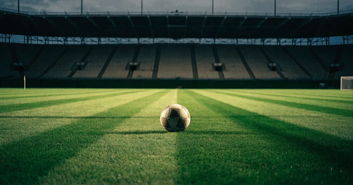Ein Fussball liegt auf dem Anstosspunkt eines frisch gemähten Rasens, dahinter eine grosse Tribüne unter bewölktem Himmel