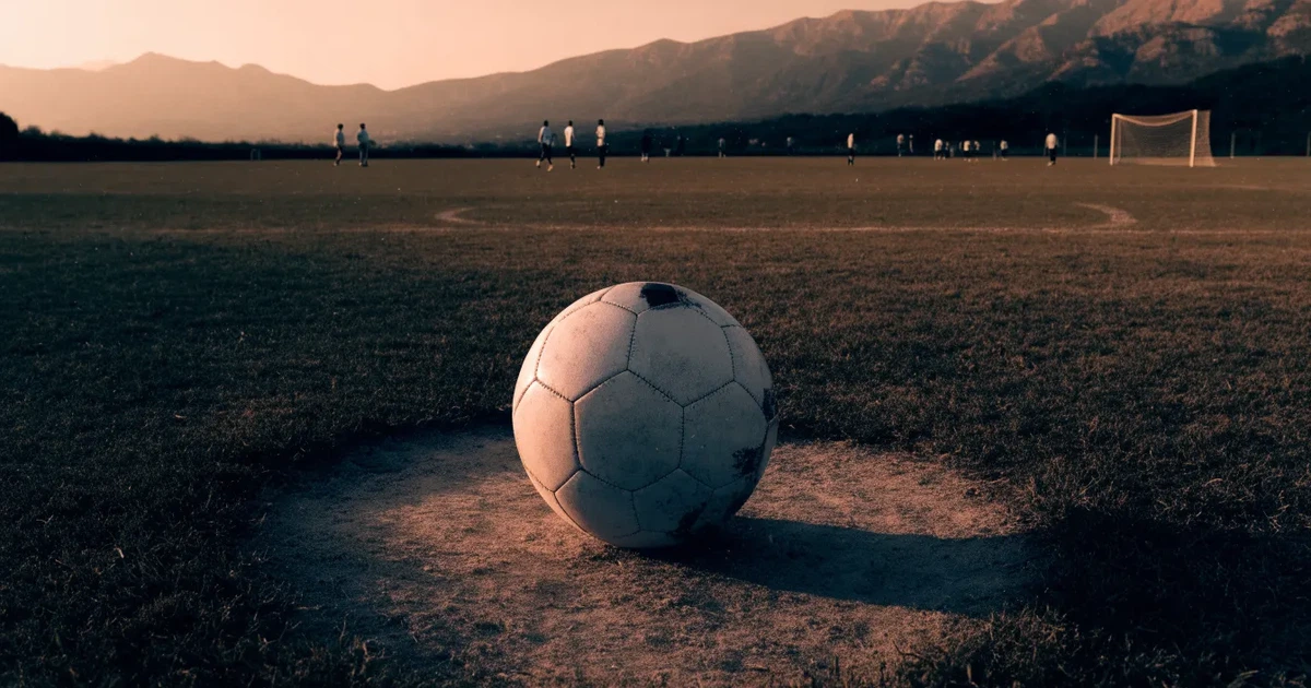 Ein Fussball auf einem staubigen Rasenstück in der Abendsonne, im Hintergrund eine hohe Bergkette