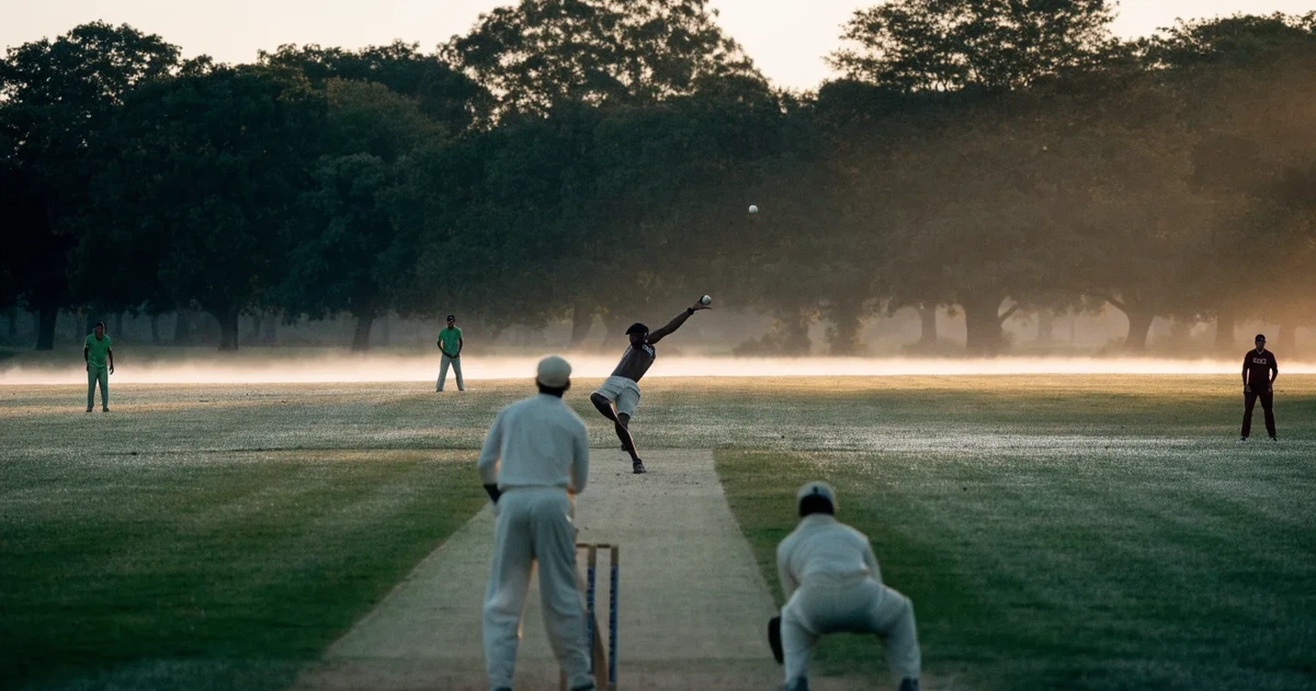 Ein ovales Cricketfeld mit gemähtem Rasen und hellem Mittelstreifen am frühen Morgen, Nebel zwischen den Bäumen am Rand