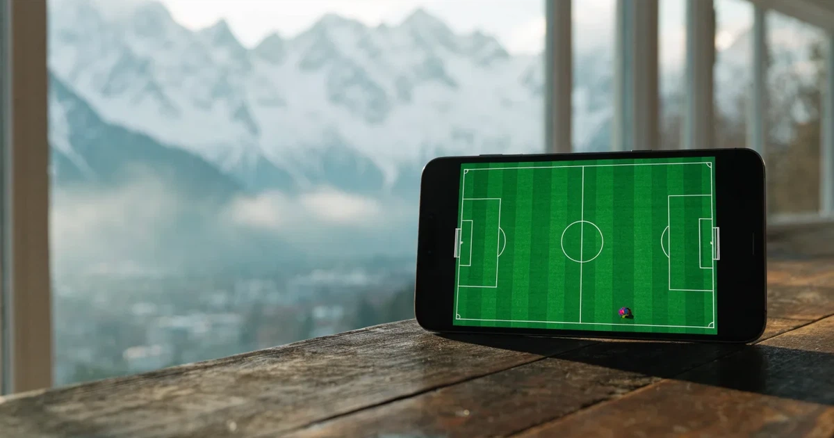 Ein Fussballplatz aus der Vogelperspektive mit sauberen Linien auf dichtem Rasen, in der Ferne verschneite Berge.