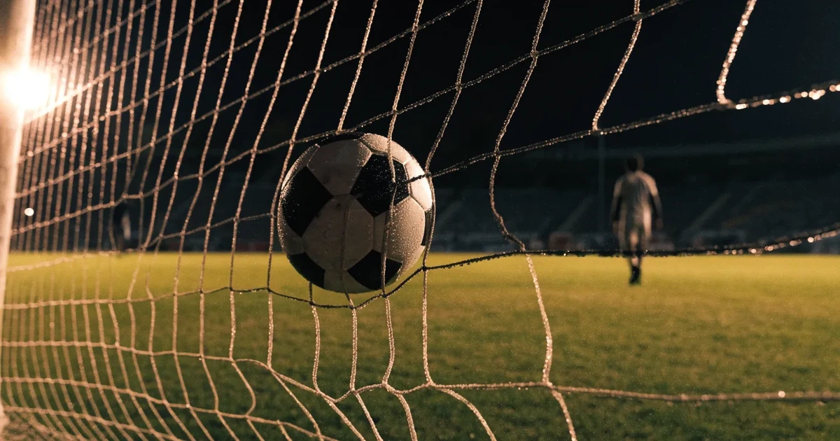 Ein Fussballnetz in Nahaufnahme, in dem ein Ball hängt, Wassertropfen glänzen auf den Maschen.