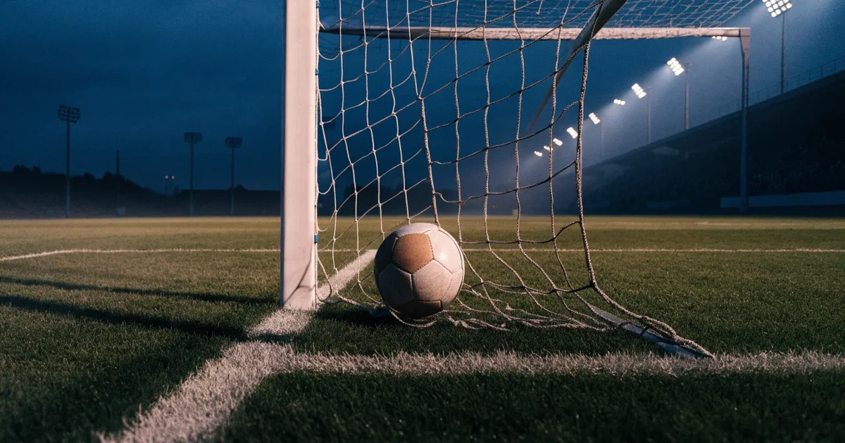 Ein Fussball liegt im Netz eines Tores, Flutlicht und kalte Abendluft liegen über dem leeren Platz